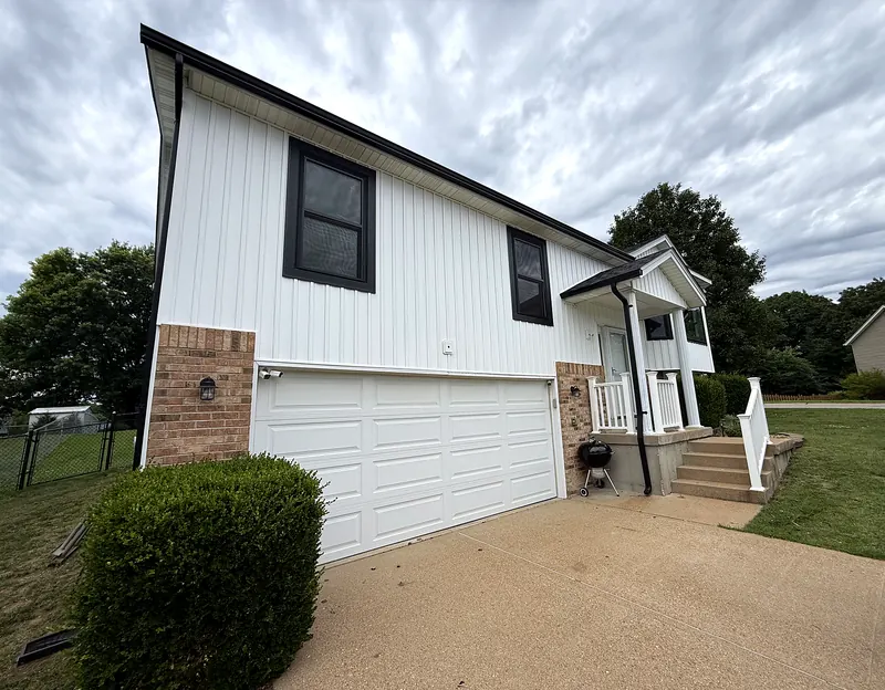 Same wall after new white vertical siding, black windows and gutters